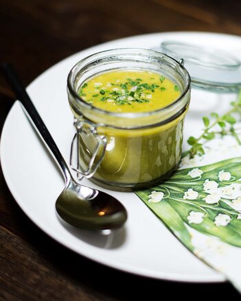 Auf dem Foto sieht man ein Glas mit veganer Gemüsesuppe. Das Einmachglas steht auf einem weißen Teller mit frühlingshafter Serviette. | © SONNENTOR