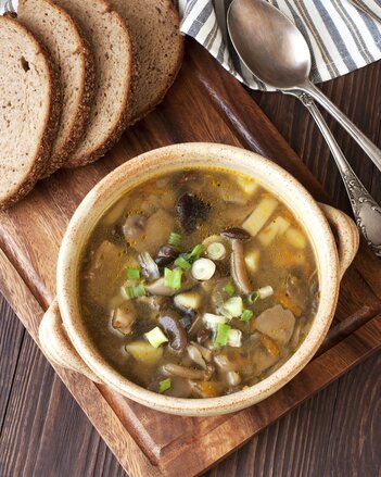 Auf dem Foto ist die Bramboracka Znaimer Kartoffelsuppe mit Pilzen auf einem Holzbrett zu sehen. Daneben liegen mehrere Scheiben Brot. | © SONNENTOR