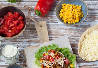 Auf dem Foto sieht man ein Holzbrett mit einem noch nicht eingerolltem Burrito. Daneben liegen Paprika, Mais, Käse, Gewürze und vieles mehr. | © SONNENTOR