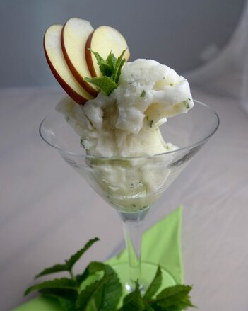 Auf dem Foto ist ein Cocktailglas mit Apfelminze-Sorbet zu sehen. Das Sorbe ist mit Apfelspalten garniert. | © SONNENTOR