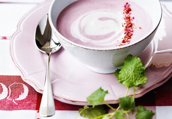 Foto von einer Tasse mit rosa Waldbeercreme. Die Creme ist mit rosa Blüten dekoriert und daneben ist Minze zu sehen. | © SONNENTOR