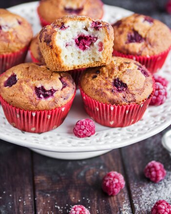 Auf dem Foto sind mehrere Himbeermuffins zu sehen. Daneben sind frische Himbeeren und Staubzucker zu sehen. | © SONNENTOR