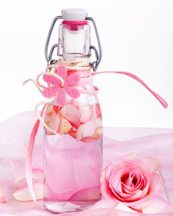 Auf dem Foto sieht man eine Flasche Rosenlikör. In der Flasche sind auch Rosenblätter zu sehen. Die Flasche steht auf einem rosa Tuch. | © SONNENTOR