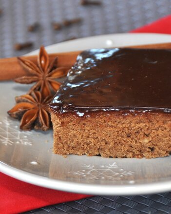 Auf dem Foto ist ein Stück Schokolebkuchen-Schnitte zu sehen. Daneben liegen zwei Sternanis und eine Zimtstange. | © SONNENTOR