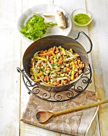 Auf dem Foto ist eine schwarze Pfanne mit bunten Wurzel-Spätzle zu sehen. Dahinter sieht man diverses Wurzelgemüse. | © SONNENTOR