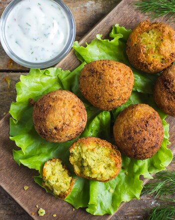 Auf dem Foto sind Falafel auf einem grünen Blatt Salat zu sehen. Daneben sieht man eine kleine Schüssel mit Gurkenraijta. | © SONNENTOR