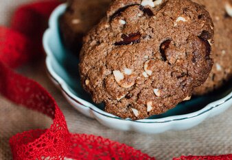 Auf dem Foto ist eine Schale mit Mandel Cookies zu sehen. Davor liegt ein satt rotes Band. | © SONNENTOR