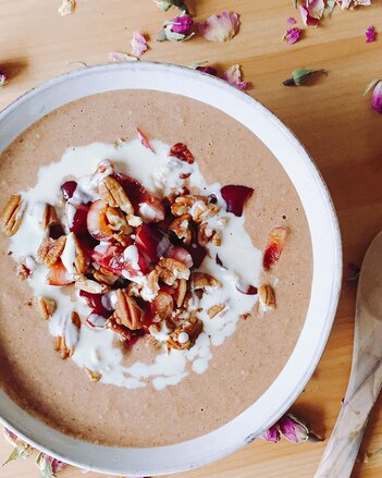 Auf dem Foto sieht man eine Schale Rosenblüten-Frappé Porridge mit Nüssen darauf. Rund um die Schüssel sind Rosenblüten verteilt. | © SONNENTOR