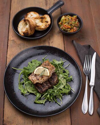 Auf dem Foto sieht man zwei Steaks auf Rucola Salat. Dahinter sind Baguettes zu sehen. | © SONNENTOR