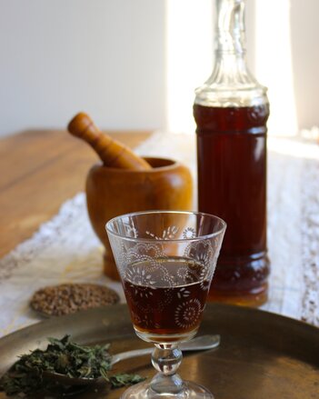 Auf dem Foto sieht man ein Shotglas mit Kräuterlikör. Dahinter sieht man eine Flasche voll mit Kräuterlikör. | © SONNENTOR