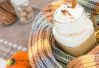 Auf dem Foto ist ein Glas Pumpkin Spice Latte zu sehen. Das Glas ist mit einem bunten Schal eingewickelt. Daneben ist ein Kürbis zu sehen. | © SONNENTOR