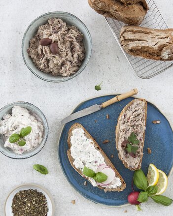 Auf dem Foto sind der Frischkäse-Basilikum und der Rosmarin-Bohnen Aufstriche zu sehen. Daneben sind zwei Scheiben Brot mit den Aufstrichen darauf zu sehen. | © SONNENTOR