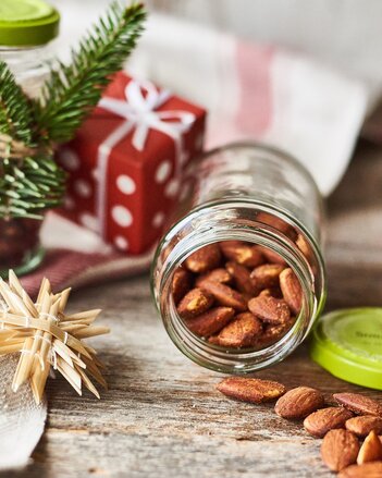 Auf dem Foto sieht man ein Glas mit süßen Gewürzmandeln. Daneben sind viele Weihnachtliche Gegenstände, wie Holzsterne, zu sehen. | © SONNENTOR