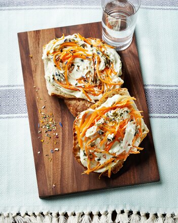 Auf dem Foto sind zwei Brotscheiben mit Kürbiskern Karotten Aufstrich zu sehen. Daneben steht ein Glas Wasser. | © SONNENTOR