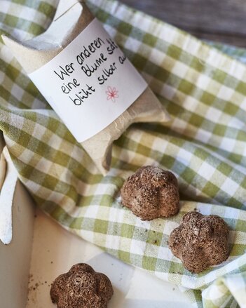 Auf dem Foto sind drei Stück Seed Bombs zu sehen. Daneben liegt eine Verpackung auf der steht: Wer anderen eine Blume sät, blüht selber auf. | © SONNENTOR