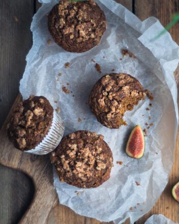 Auf dem Foto sind Kurkuma Muffins mit Karotten und Äpfeln zu sehen. Von einem Muffin wurde bereits abgebissen. Daneben liegt eine Feige. | © SONNENTOR