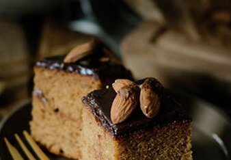 Auf dem Foto sind zwei Stück Weihnachtlicher Gewürzkuchen zu sehen. Er hat eine Schokoglasur und darauf sind Mandeln zu sehen. | © SONNENTOR