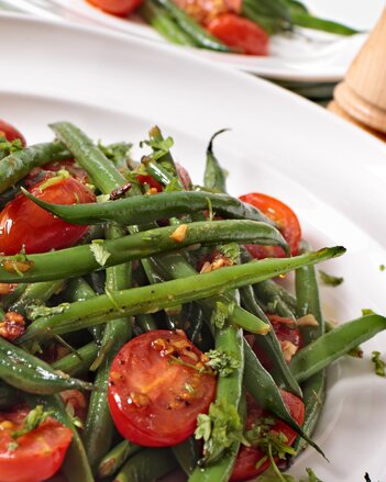 Auf dem Foto ist ein Fisolensalat mit Tomaten zu sehen. Dahinter sieht man noch einen zweiten Teller mit Fisolen-Tomaten Salat. | © SONNENTOR