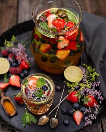 Auf dem Foto ist ein Krug und ein Glas gefüllt mit Kurkuma Beeren Bowle zu sehen. Darin sind zahlreiche Früchte und Beeren zu sehen. | © SONNENTOR