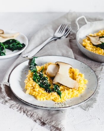 Auf dem Foto ist ein Teller mit Kürbisrisotto zu sehen. Das Risotto ist mit Steinpilzen und Blattspinat angerichtet. | © SONNENTOR