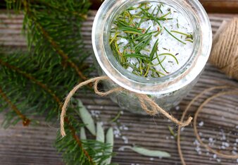 Auf dem Foto ist ein Schälchen mit dem Waldbadesalz zu sehen. Darauf sind Fichtennadeln verteilt. Um das Glas herum sind auch Fichtenzweige verteilt. | © Valerie Jarolim