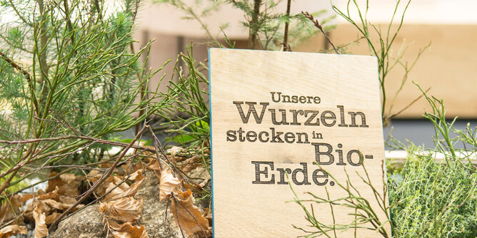 Auf dem Foto ist eine Holztafel zu sehen. Darauf stehen die Worte - Unsere Wurzeln stecken in Bio-Erde. | © SONNENTOR