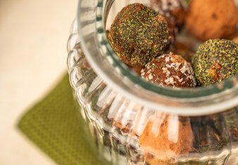 Die Bliss Balls sind gemischt in ein offenes Glas gefüllt, welches auf einer grünen Stoffserviette steht.  | © SONNENTOR