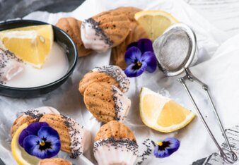 Auf dem Foto sind mehrere Zitronen-Mohn-Madeleines zu sehen. Daneben sieht man Blüten. | © SONNENTOR