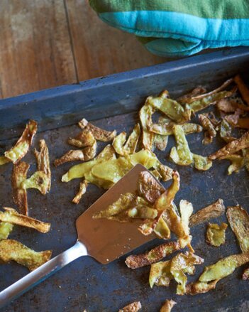 Auf dem Foto sind Kartoffelschalen Chips auf einem Blech zu sehen. Neben dem Blech liegt ein Backhandschuh. | © SONNENTOR