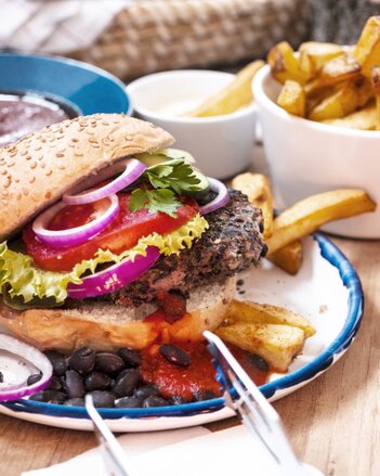 Auf dem Foto sieht man einen Burger mit veganem Patty. Daneben sieht man eine Schale mit Pommes. | © SONNENTOR