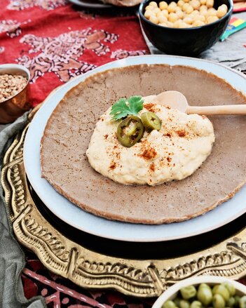 Auf dem Foto sieht man Injera mit Shiro darauf. Im Hintergrund ist eine Schüssel mit Kichererbsen zu sehen. | © SONNENTOR