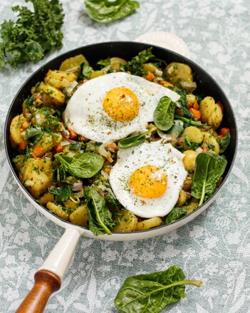 Auf dem Foto sieht man eine Pfanne mit Veggie Gröstl. Darauf sind zwei Spiegeleier und Babyspinat zu sehen. | © SONNENTOR