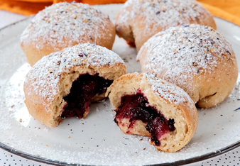 Auf dem Foto sind vier fruchtige Mini-Ofenkrapfen zu sehen. Eine ist in der Mitte geteilt, sodass man den Fruchtaufstrich sehen kann. | © SONNENTOR