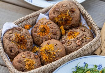 Auf dem Foto sind Walnuss-Brötchen mit Ringelblumen darauf zu sehen. Die Brötchen liegen in einem Korb. | © SONNENTOR