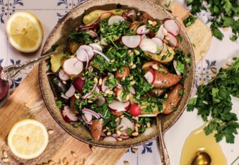 Auf dem Foto ist eine Schüssel mit Kartoffel-Radieschen Salat zu sehen. Die bunte Bowl steht auf einem Holzbrett. Daneben sind Pinienkerne zu sehen. | © SONNENTOR