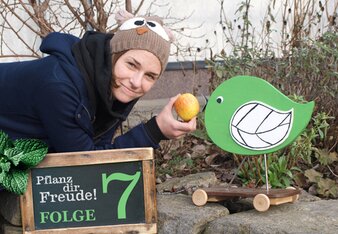 Aufdem Foto sieht man eine Frau mit einem Apfel in der Hand. Davor sieht man einen Holzvogel. | © SONNENTOR