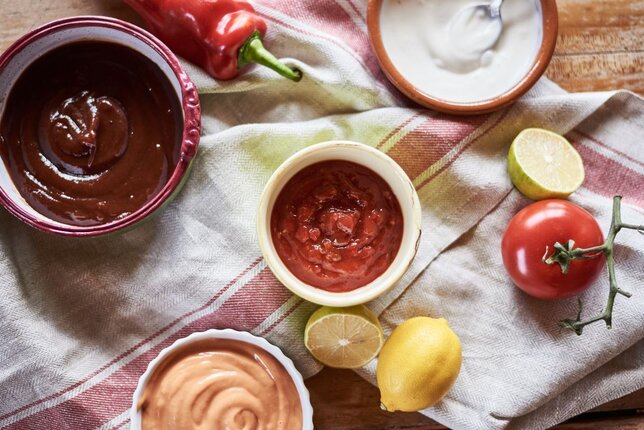 Auf dem Foto sind vier Schälchen mit unterschiedlichen BBQ Saucen zu sehen. Daneben sieht man Zitronen, Paprika und Tomaten. | © SONNENTOR