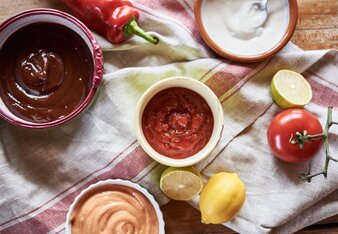 Auf dem Foto sind vier Schälchen mit unterschiedlichen BBQ Saucen zu sehen. Daneben sieht man Zitronen, Paprika und Tomaten. | © SONNENTOR