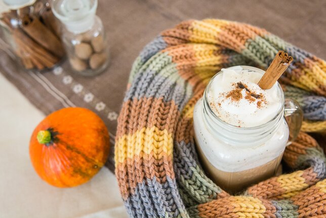 Auf dem Foto ist ein Glas mit Pumpkin Spice Latte zu sehen. Das Glas ist mit einem Schal umhüllt. Daneben liegt ein kleiner Kürbis. | © SONNENTOR