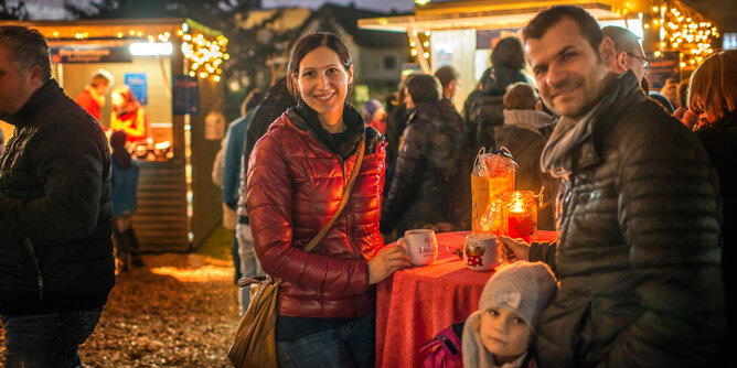 Auf dem Foto sieht man eine Familie auf einem Adventmarkt. Die Eltern halten jeweils eine SONNENTOR Tasse in den Händen. | © SONNENTOR