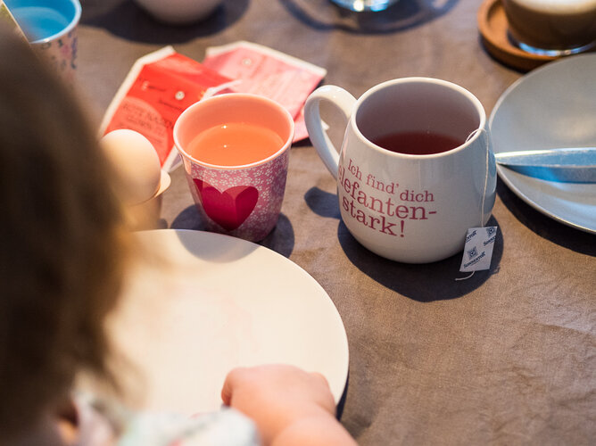 Auf dem Foto sieht man ein Kind vor einem Teller und einer Tasse Tee sitzen.  | © SONNENTOR